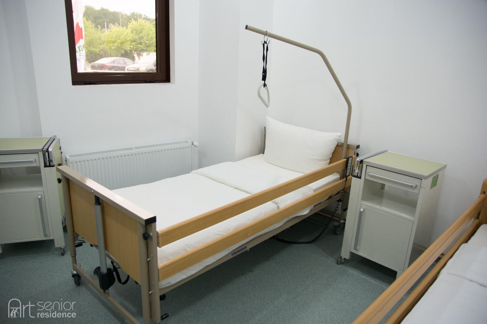 Cameră cu două paturi medicale, noptieră și fereastră