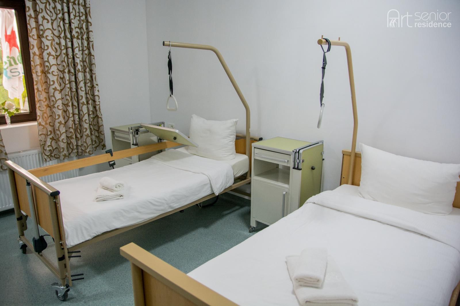 Cameră luminoasă cu două paturi medicale reglabile și fereastră cu draperii