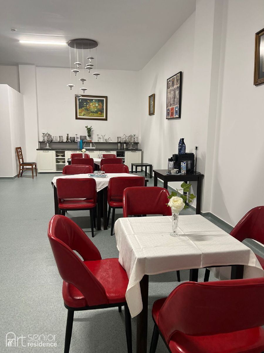 Sala de mese cu fețe de masă albe și scaune roșii tapițate